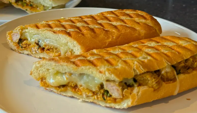 Close-up of a grill-marked panini cut in half, melted cheese and spiced chicken spilling from the middle