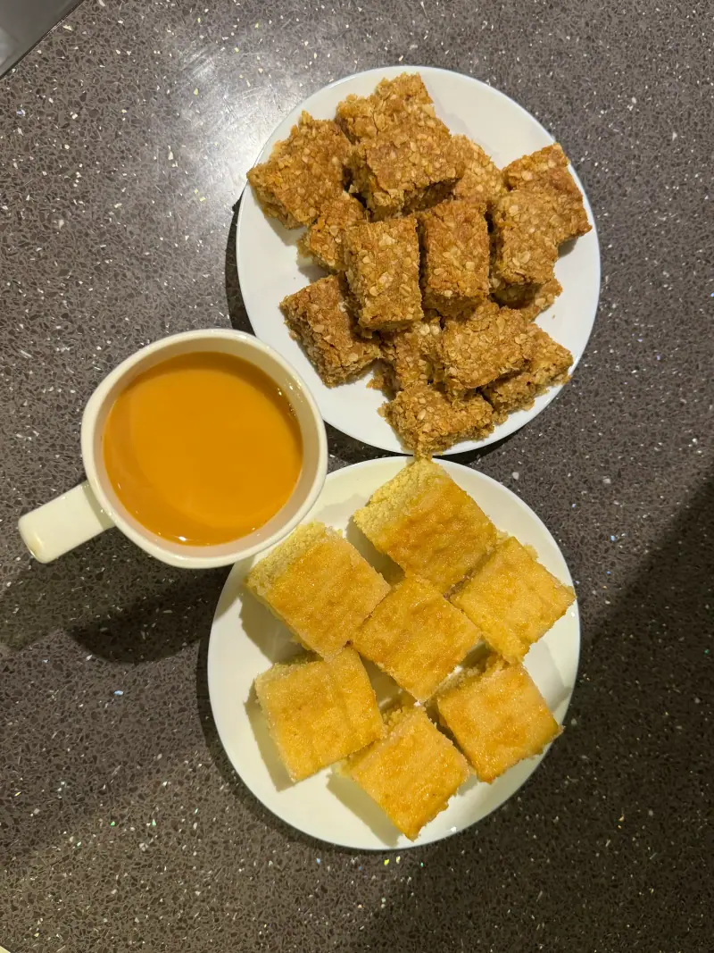 Two plates of homemade traybake squares beside a cup of tea